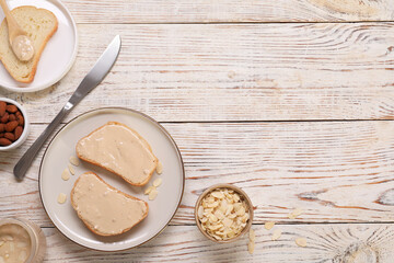 Toasts with tasty nut butter and almonds on light wooden table, flat lay. Space for text
