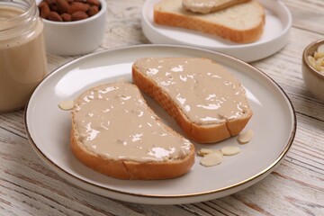 Toasts with tasty nut butter and almond flakes on light wooden table, closeup