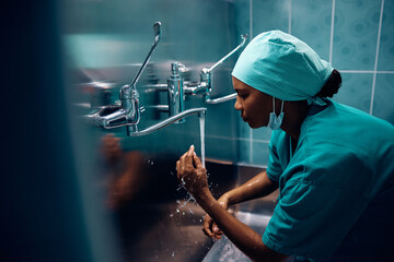Black female doctor washing her hands before surgery in hospital. - obrazy, fototapety, plakaty