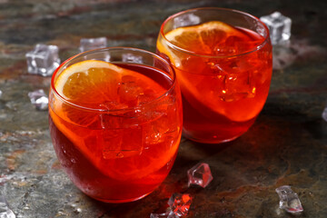 Aperol spritz cocktail, ice cubes and orange slices in glasses on grey textured table, closeup