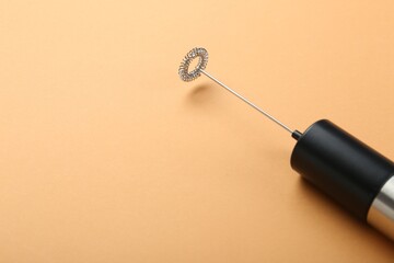 Milk frother wand on pale orange background, closeup. Space for text