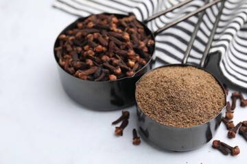 Aromatic clove powder and dried buds in scoops on white table, closeup