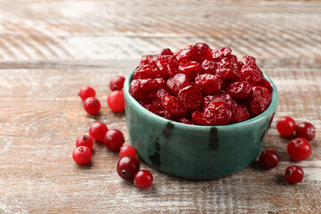 Tasty dried cranberries in bowl and fresh ones on rustic wooden table, closeup. Space for text