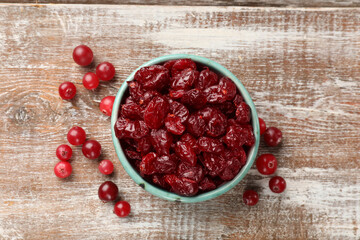 Tasty dried cranberries in bowl and fresh ones on rustic wooden table, top view