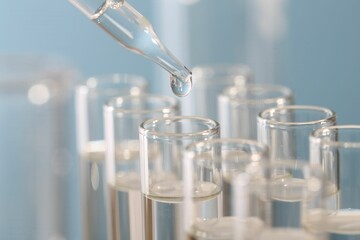 Laboratory analysis. Dripping liquid from pipette into glass test tube on blurred background, closeup