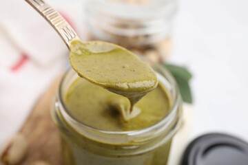 Taking tasty pistachio cream with spoon from jar at white table, closeup