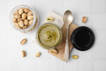Tasty pistachio cream and nuts on white tiled table, flat lay