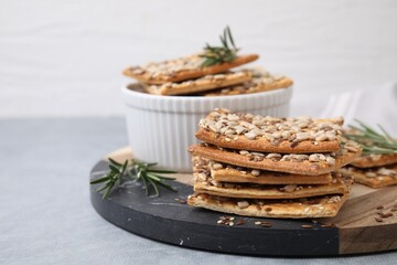 Cereal crackers with flax, sunflower, sesame seeds and rosemary on grey table, closeup