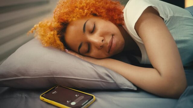 Young woman sleeps in bed, ignoring call from boss in the morning, late for work