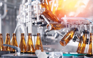 Closeup brown bottles for beer on modern, automated bottling production line in brewery. Process pasteurization, Germ removal and glass cleaning
