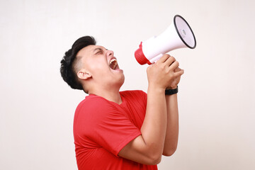 Handsome Asian young man screaming using megaphone. Isolated on white