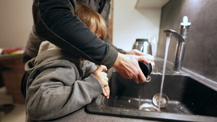 Mother and child washing dishes in kitchen sink, family lifestyle scene of little boy helping mom...
