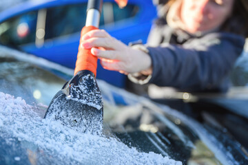 Woman deicing car windshield with ice scraper
