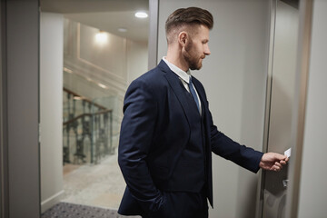 Side view portrait of successful young businessman opening hotel room door with key card, copy space