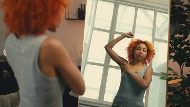 Young woman unsatisfied with her underarm skin condition in front of a mirror