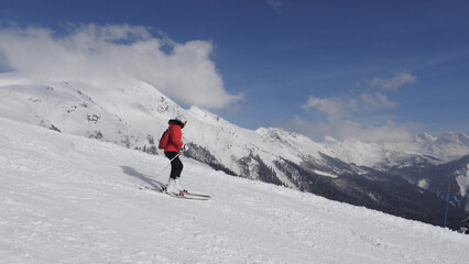 Naklejka na ściany i meble Active skier skiing down snowy slope in mountains at ski resort. Adrenaline is in blood from speed and breathtaking mountain scenery with snow capped summits and glaciers. Winter recreation and sports