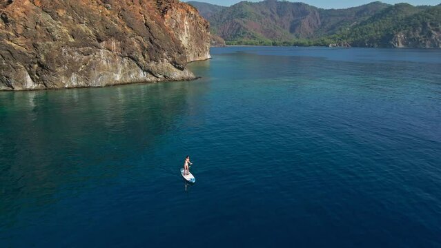 Aerial view of young woman in bikiny using long paddle for floating on sup board in Mediterranean sea