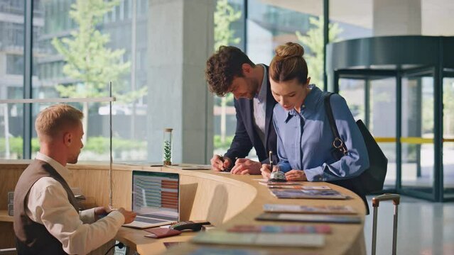 Clients writing hotel papers at reception lobby. Young couple tourists check in