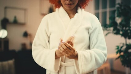 Young woman in bathrobe applying moisturizing hand cream, beauty rituals, care
