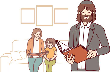 Orthodox jewish man stands near wife and daughter and holds bible book with prayers in hands. Religious bearded jewish guy in kippah smiles and looks at screen, located in apartment