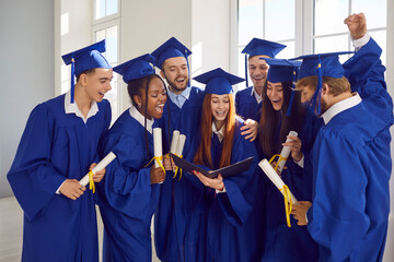Multinational group of high school or academy graduates displays diplomas. Clad in mortarboards and...