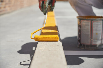 Paint roller being used to apply yellow paint on a kerbstone for road marking on a parking lot..
