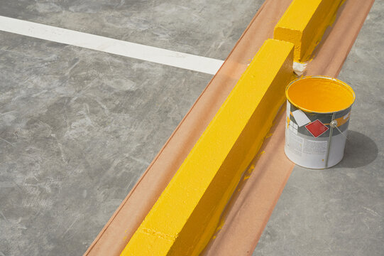 Parking lot marking paint. Paint bucket next to kerbstone recently painted with yellow acrilyc paint.