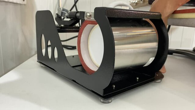 Male hand making a personalised white glass coffee mug with heat press printing machine.
