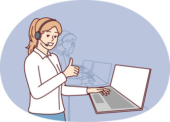 Woman in headphones for call center stands near laptop and looks at camera showing thumbs up. Girl employee of psychological support service or software user consultation smiling