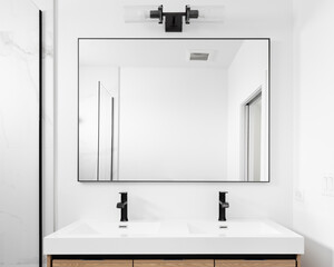 A modern bathroom with a wood cabinet, a black light above a large rectangular mirror, and a marble shower.