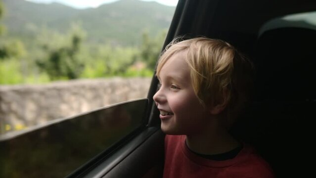 Preteen boy look out through window of car during family road trip and enjoy of pleasant expectation of happy vacation. Glad child travel with parents while holidays. Journey through the countryside