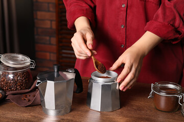Woman putting ground coffee into moka pot at wooden table, closeup