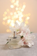 Bottle of perfume and beautiful lily flowers on table against beige background with blurred lights