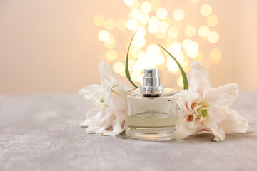 Bottle of perfume and beautiful lily flowers on table against beige background with blurred lights, space for text