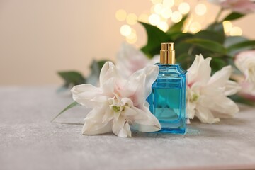 Obraz na płótnie Canvas Bottle of perfume and beautiful lily flowers on table against beige background with blurred lights, closeup. Space for text