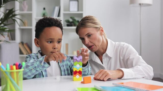 Assessment of mental development of children. Professional psychologist observes small multiracial boy playing with puzzle game, assessing his readiness for preschool. Exercises for kid with autism.