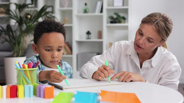 Adorable little african american boy with curly hair having fun at pediatric specialist appointment, happy child drawing with female therapist, exercises for children with autism.