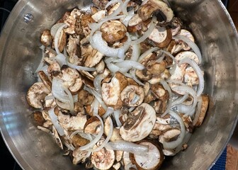 A pot full of sliced portobello mushrooms and onions ready to sauté