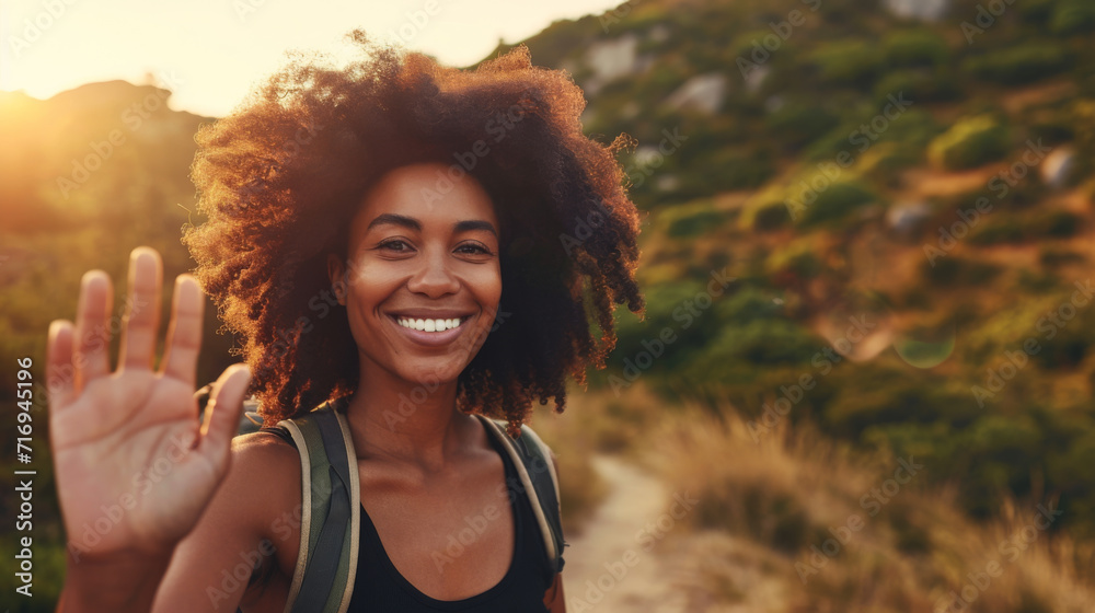 Poster cheerful young woman with a backpack is waving at the camera, with a sunlit natural landscape in the background