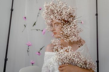 Portrait of sensual blond woman with flowers. Beautiful girl with flowers in her hair. Summer Beauty. Art in a contemporary style. A gypsophila wreath on a white background. Perfume, cosmetics concept