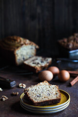 Slices of fresh homemade banana bread on a stack of saucers with ingredients nearby. Selective focus with blurred foreground and background.