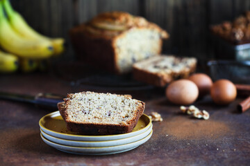 Slices of fresh homemade banana bread on a stack of saucers with ingredients nearby. Selective focus with blurred foreground and background.