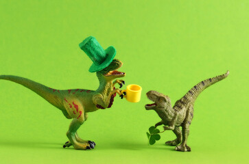 Fototapeta premium Two green dinosaurs in green hats with beer and clover leaf celebrating St. Patrick's day. Unusual festive card.