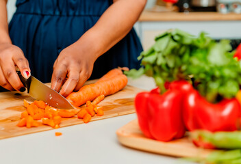 Detalle de las manos de una mujer africana o afroamericana cortando verdura en la tabla de la cocina