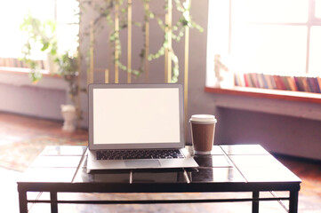Photo of white blank screen of laptop with keyboard lying on wooden little table with cup of coffee