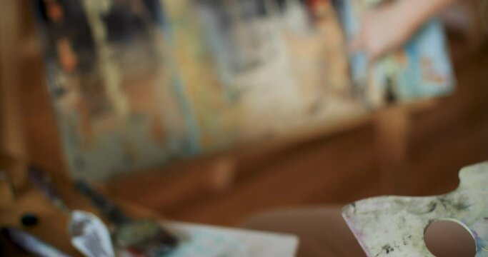 Closeup of artist painting with palette knife on canvas. Female painter is using oil paints. She is working at art studio. 