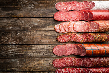 Set of different types of sausages, salami and smoked meat with basil and spices on wooden background. Top view.