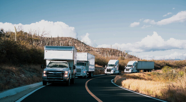 Convoy of white trucks with containers on the road, cargo transport concept, at dusk.
