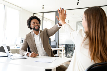A high-five between a man and woman in an office signifies a celebratory moment of success or...
