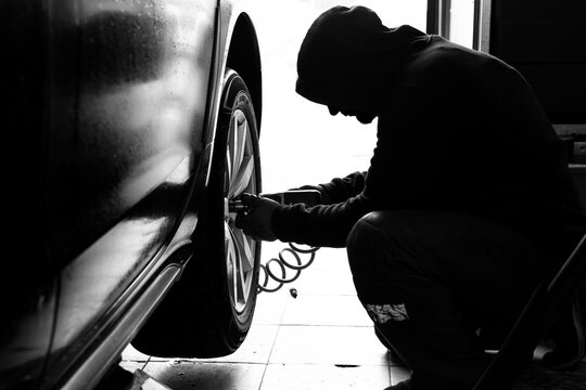 Mechanic at a car service center unscrews a wheel from a car using a pneumatic tool